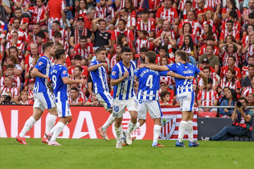 El centrocampista del Alavés Denis Suárez (2d) celebra marcar el primer gol de su equipo, durante el partido de la cuarta jornada de LaLiga EA Sports que Athletic Club y Deportivo Alavés disputan este sábado en el estadio de San Mamés. EFE/Javier Zorrilla
