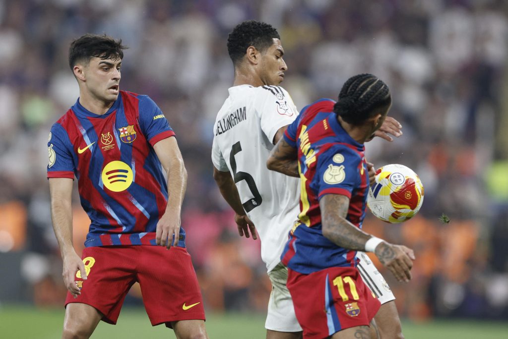 Los jugadores del FC Barcelona Pedri (i) y Raphinha (d) disputan un balón con el centrocampista del Real Madrid Jude Bellingham (c). EFE/ Kai Försterling
