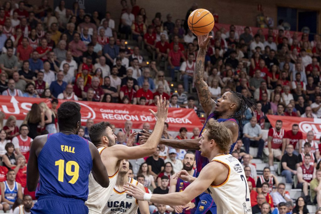 El alero del Barcelona Will Clyburn (d) lanza a canasta ante el pívot de UCAM Murcia Emanuel Cate (2i), durante el tercer partido de cuartos de final de la Liga Endesa que Barcelona y UCAM Murcia están disputando este sábado en el Palacio de los Deportes de Murcia. EFE/Marcial Guillén
